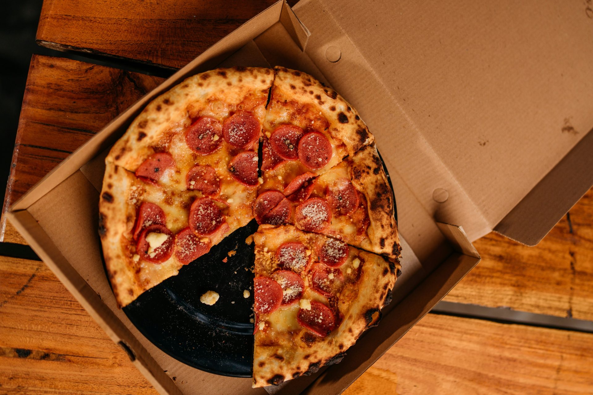 Pepperoni pizza in a cardboard box on a wooden table